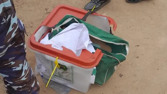 Ballot box dey for ground wit electoral materials inside wit police pipo leg near am