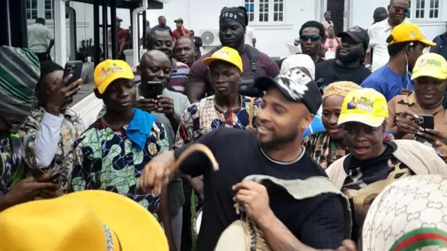 B-Red dey play di traditional yoruba Talking Drum as e dey celebrate im papa victory wit pipo