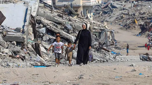 Umugore w’Umunye-Palestine arimo kugenda n’amaguru ari kumwe n’abana, bari mu muhanda ukikijwe n’ibirundo by’ibyasenyutse, mu gace ka Sheikh Radwan, ko mu mujyi wa Gaza