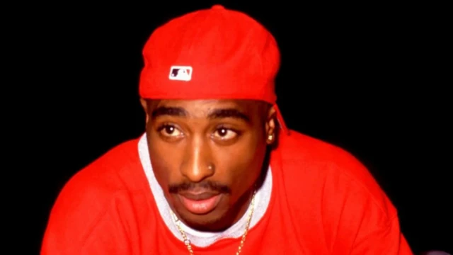 Tupac Shakur yambaye imyenda isa umutuku mo imbere yambayemo umweru n'ingofero y'umutuku