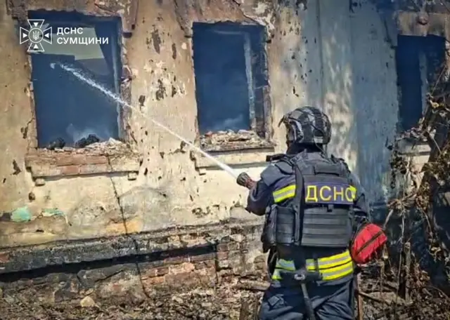 Работник ГСЧС тушит поврежденное здание