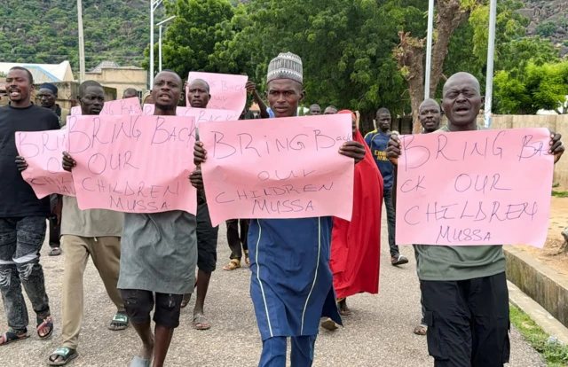 Ababyeyi b'abana bashimuswe bari kugenda mu muhanda bafite impapuro zanditseho ngo" Mugarure abana bacu"