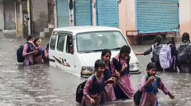 दिल्ली के संगम विहार इलाक़े में फंसी वैन. यहां स्कूली छात्राएं घुटने से ऊपर तक जमा पानी में सड़क पार करती दिख रही हैं.