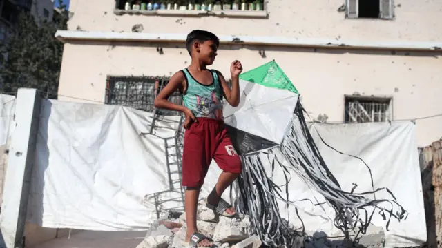 ፍልስጤማዊ ሕጻን እሁድ ዕለት ጋዛ ከተማ የተፈናቃይ ካምፕ ውስጥ ካይት ይዞ ፎቶ ተነስቷል