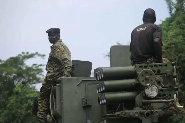 Abasirikare babiri ba Uganda bari hejuru y’imbunda ya rutura. Umwe muri bo yambaye impuzankano ya gisirikare, mu gihe undi yambaye umupira w’amaboko magufi w’igikara wanditseho amagambo “UPDF”.