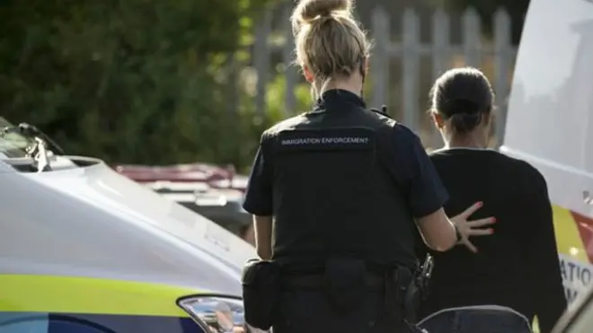 Viên chức di trú bắt một di dân bất hợp pháp trong một cuộc truy quét ở during raid in Slough, Berkshire, Anh Quốc.