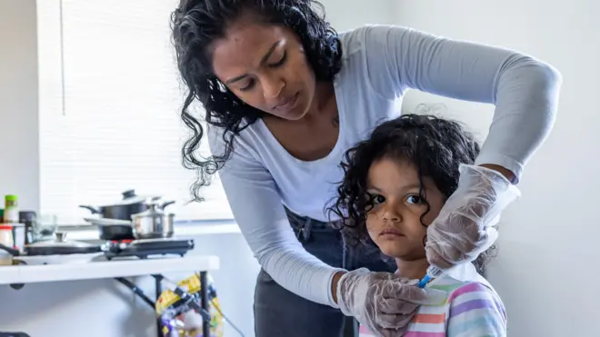 Como parte de su rutina diaria, Deysi Vargas limpia con una solución salina el cateter intravenoso de su hija antes de su ducha matutina y la escuela. Fotografiada en Bakersfield, California, Estados Unidos, el viernes 23 de mayo de 2025. (Myung J. Chun / Los Angeles Times a través de Getty Images).