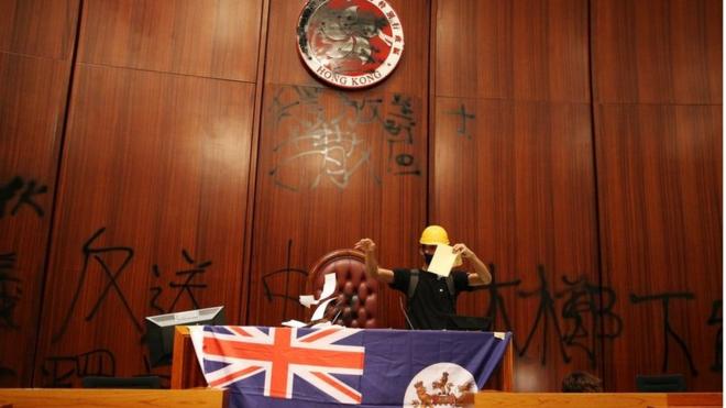 示威者在香港立法會會議廳塗污區徽，展示港英旗幟。