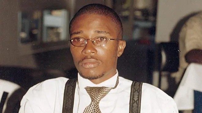 Floribert Bwana Chui Bin Kositi yambaye indorerwamo n'ishati y'umweru iriho imirongo ibiri y'ikigina ku mpande zombi, na karuvati ijya kuba ikigina