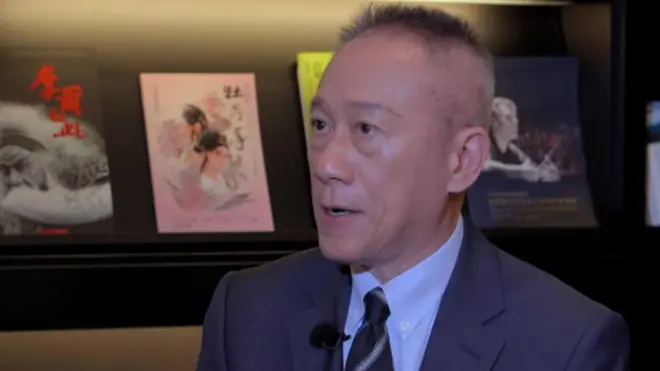 TSMC's Wendell Huang wearing a suit and sitting for an interview, with pictures or books seen on the wall behind him