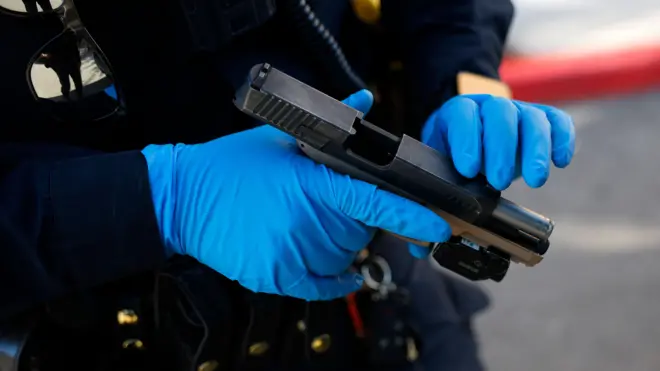 Ìbọn tí èèyàn kan tó wọ ìbọ̀wọ́ olómi aro mú dání