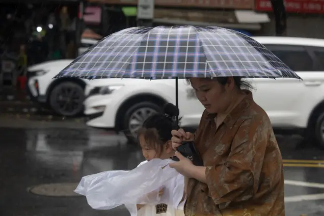 颱風巴威逼近,中國浙江溫州街頭一位女士撐起雨傘帶著一位女孩走過街頭(11/7/2026)