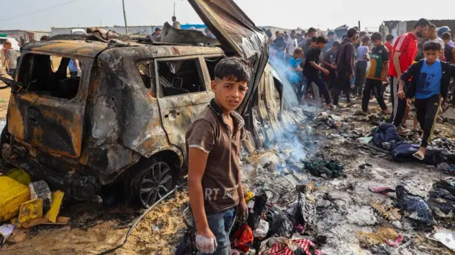 A boy looking over burned out vehicle 