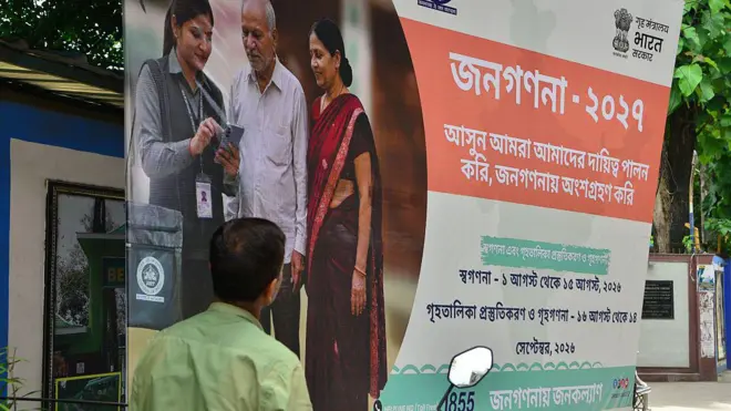 জনগণনা-সংক্রান্ত পোস্টারের সামনে দাঁড়িয়ে এক ব্যক্তি 