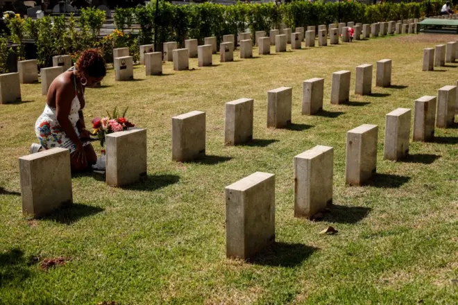 Uma mulher ajoelhada perto de um túmulo em um cemitério