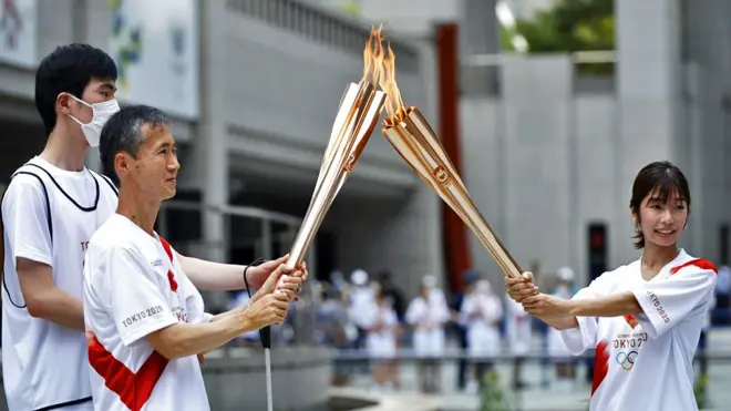 Torchbearers light the Olympic torch and pass the flame around to one another in Shinjuku District in Tokyo, Japan, on 23 July 2021