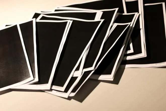 ページが全て黒塗りされた資料の紙がたくさん机の上に並んでいる