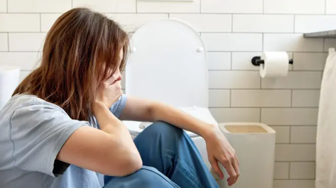 tuvalette oturan ve eliyle ağzını tutmuş hasta bir kadın