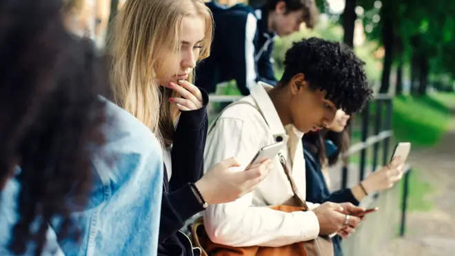 Stock photo shows teens outside looking at phones