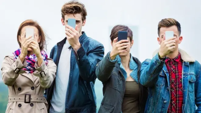 Cuatro personas jóvenes sostienen teléfonos inteligentes frente a sus caras