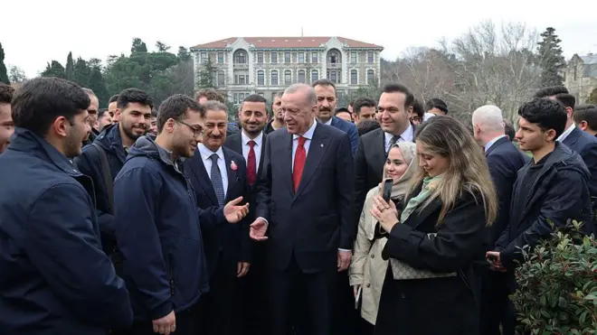 Cumhurbaşkanı Erdoğan yanında çok sayıda genç ve arkasında korumalarıyla birlikte Boğaziçi Üniversitesi kampüsünün bahçesinde. Arkada okulun binalarından biri gözüküyor