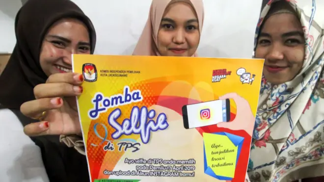 Warga menunjukkan selebaran sosialisasi lomba "Selfie di TPS" pemilu serentak 2019 di Lhokseumawe, Aceh, Minggu (14/04).