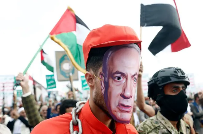 متظاهرون مؤيدون لجماعة الحوثي في اليمن يسيرون في متظاهرة بينما وضع أحدهم قناعا بصورة رئيس الوزراء الإسرائيلي بنيامين نتايناهو وارتدى لباس مطلوب للعدالة