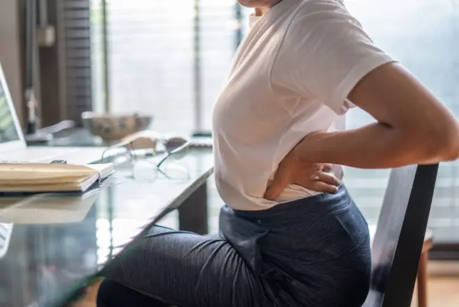 Une femme souffrant de maux de dos, assise à son bureau à domicile, travaille à son bureau d'ordinateur.