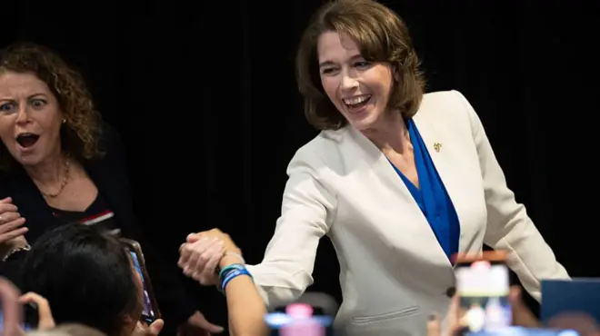 Crawford, con chaqueta blanca, le da la mano a una de sus seguidoras y sonríe 