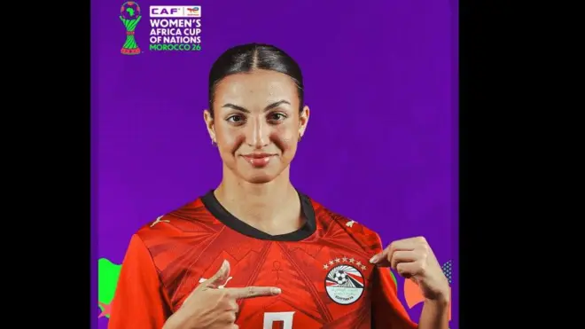 لاعبة لون بشرتها حنطي وترتدي قميص المنتخب المصري للرجال باللون الأحمر، وعليه شعار الاتحاد المصري وفوقه سبع نجوم.