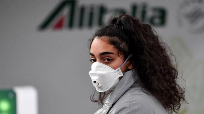 A passenger wearing a respiratory mask looks on as she waits at the Terminal T1 of Rome's Fiumicino international airport