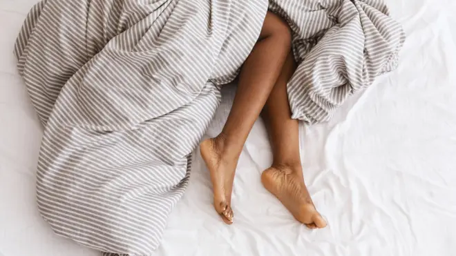 Dos piernas sobresalen de un edredón de rayas en una cama