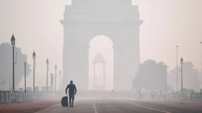 A man with a suitcase walks towards Delhi's India Gate shrouded in smog