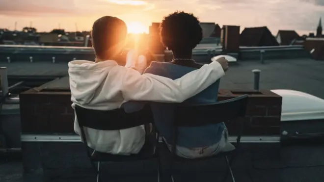 Una pareja mira el atardecer desde el techo de un edificio