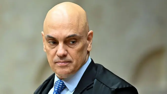 Alexandre de Moraes con la mirada baja y gesto serio, viste chaqueta, camisa azul claro y una corbata también azul