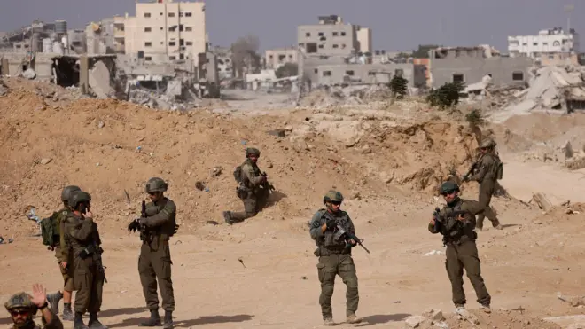 جنود إسرائيليون يقفون حراساً بينما تظهر في الخلفية مبانٍ متضررة، وسط العملية البرية المستمرة للجيش الإسرائيلي ضد حركة حماس