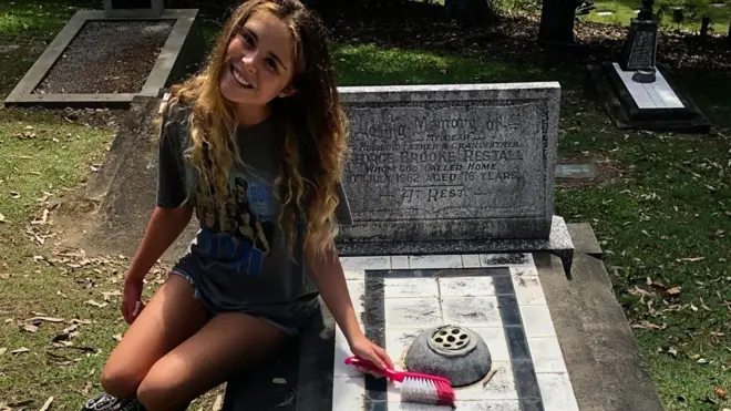 ታዳጊዋ ከማጽጃ ብሩሽዋ ጋር መቃብር ላይ ተቀምጣ