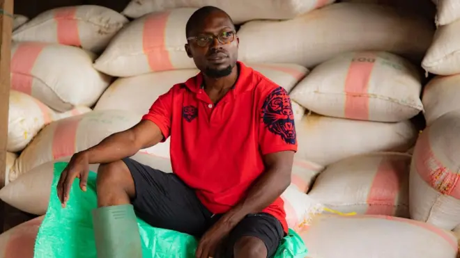 Loic Kamwa sur des sacs de mais dans son magasin