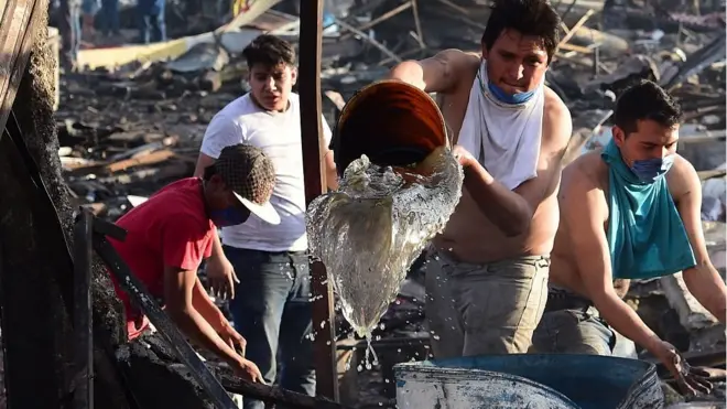 Personas vecinas del mercado de San Pablito ayudan a apagar las llamas tras la explosión.