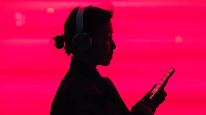 Woman in silhouette listening to music on smarphone in front of a bright pink background