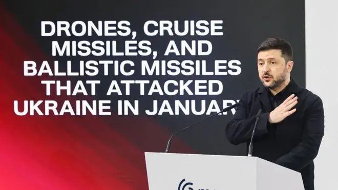 Зеленский на трибуне Мюнхенской конференции, рядом на огромном экране надпись на английском "дроны, крылатые ракеты и баллистические ракеты, которые атаковали Украину в январе"
