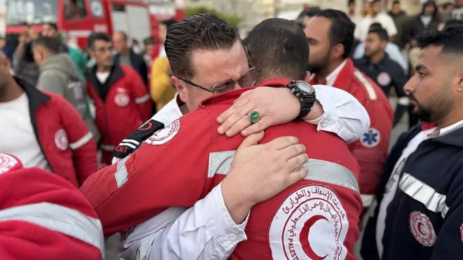 Funcionários do Crescente Vermelho Palestino se abraçam enquanto transferem os corpos de seus colegas para Khan Yunis, no sul de Gaza