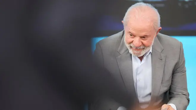 Lula, sentado, olha para o canto inferior esquerdo da imagem