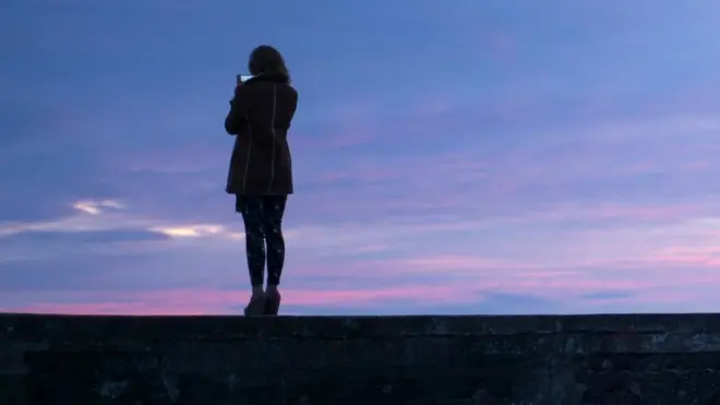 امرأة تصور الغروب بهاتف محمول