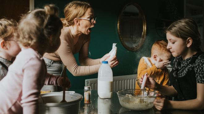 Famíliaroleta sorteio de nomespessoas brancas e loiras na cozinha, a mãe segura algo nas mãos e a criança pequena chora 