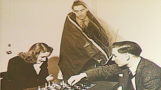 Voluntarios en el experimento jugando ajedrez mientras otro observa cubierto con una bolsa