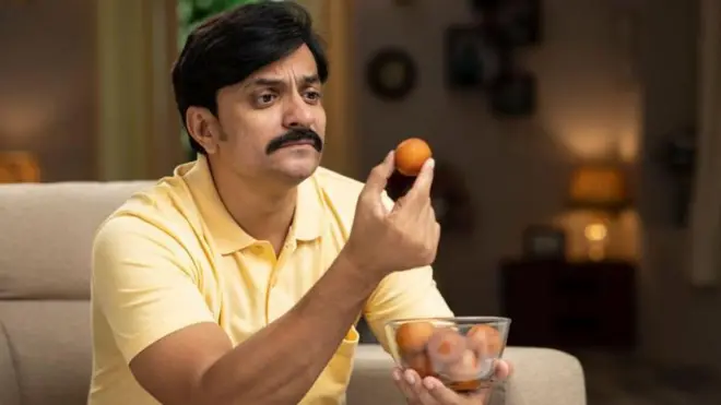 స్వీట్ చేతిలో పట్టుకుని ఆలోచిస్తున్న వ్యక్తి