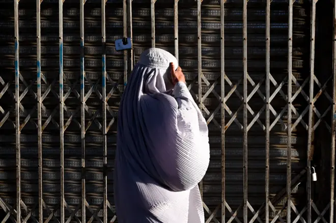 An Afghan burqa-clad woman walks past a closed shop at a market in Kandahar on 25 August 2024