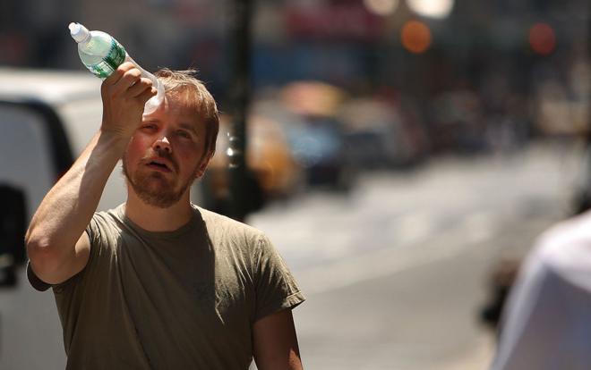 Hombre con calor sostiene una botella de agua congelada sobre su frente