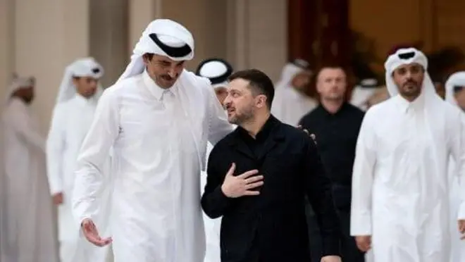 Зеленский идет и беседует с эмиром Катара, шейхом Тамимом бин Хамадом Аль-Тани. Тот, будучи гораздо выше, обнимает Зеленского за плечо 